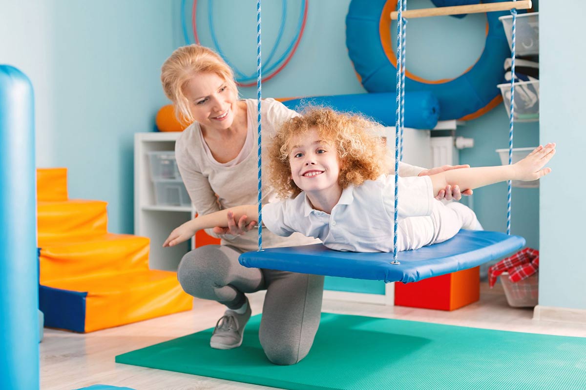 Εργοθεραπευτής κάνει ασκήσεις ισορροπίας σε παιδί που χρειάζεται εργοθεραπεία